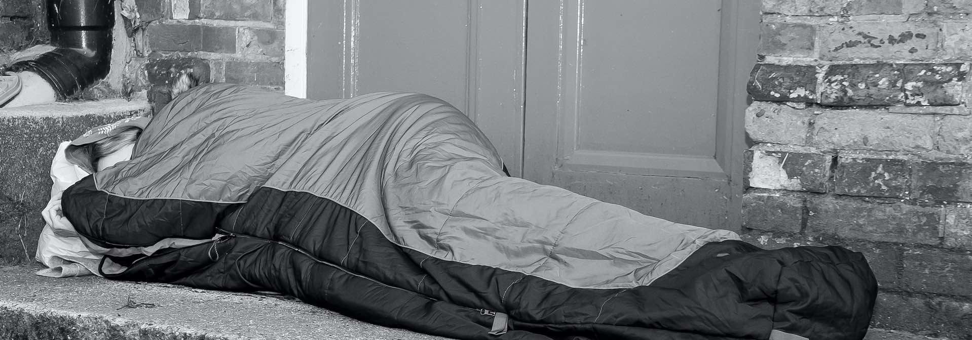 Homeless person lying in a sleeping bag in a doorway
